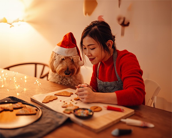 Dog in a santa hat baking cookies with a woman in an apron