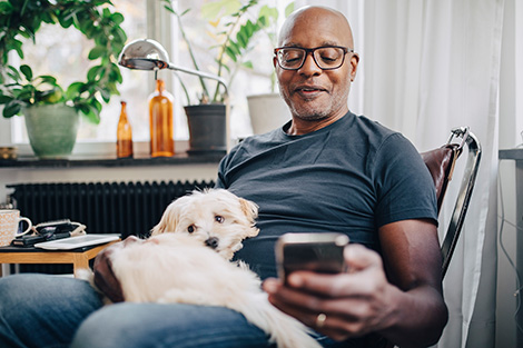 An African American older man checking his phone while holding a dog on his lap.