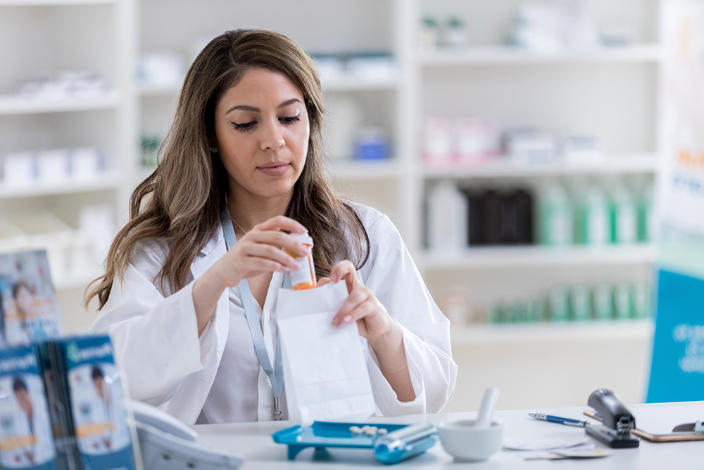 Pharmacist placing a prescription bottle in a bag.