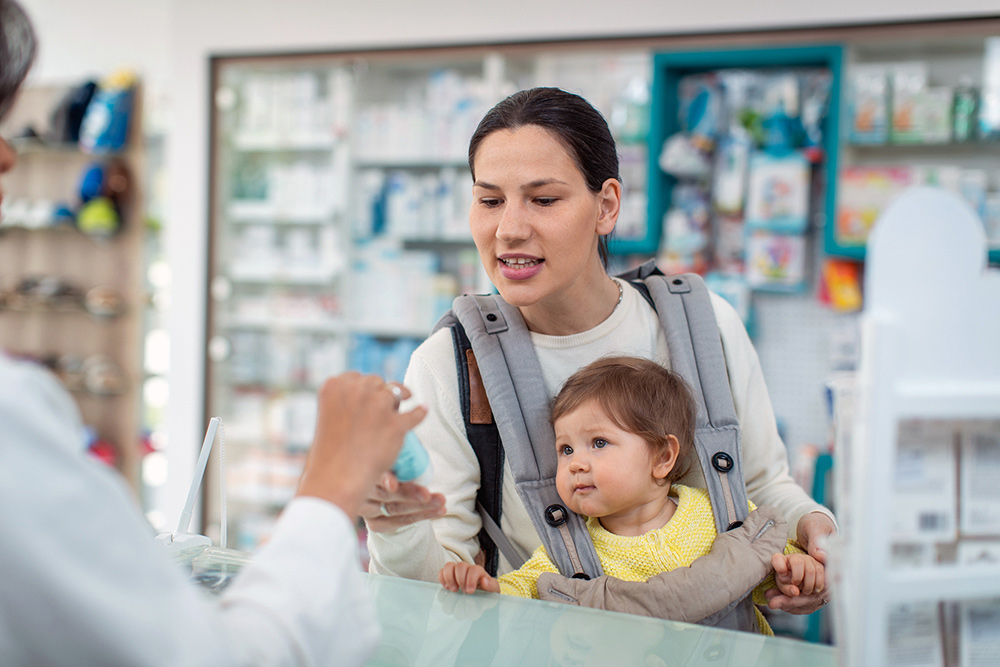 Madre con su bebé pasando por caja en una farmacia.