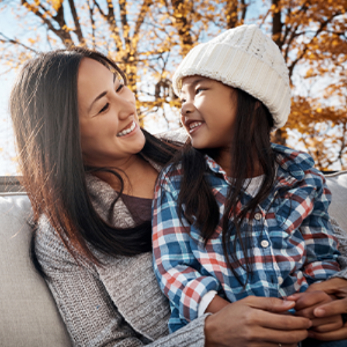 Mujer y su hija sonriendo al aire libre.