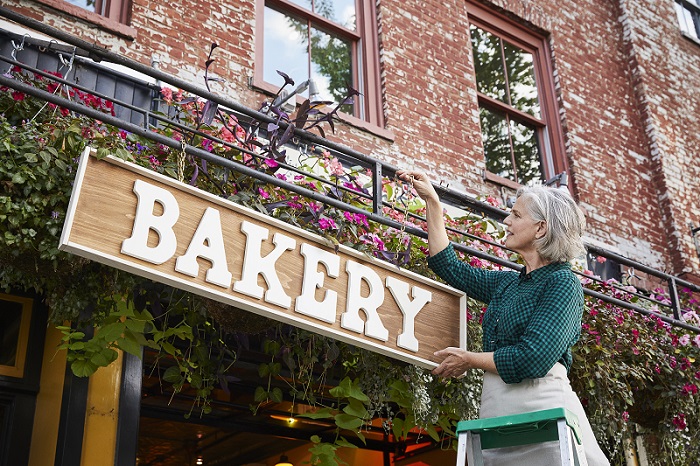 Woman hanging a bakery sign on the outside of a brick building