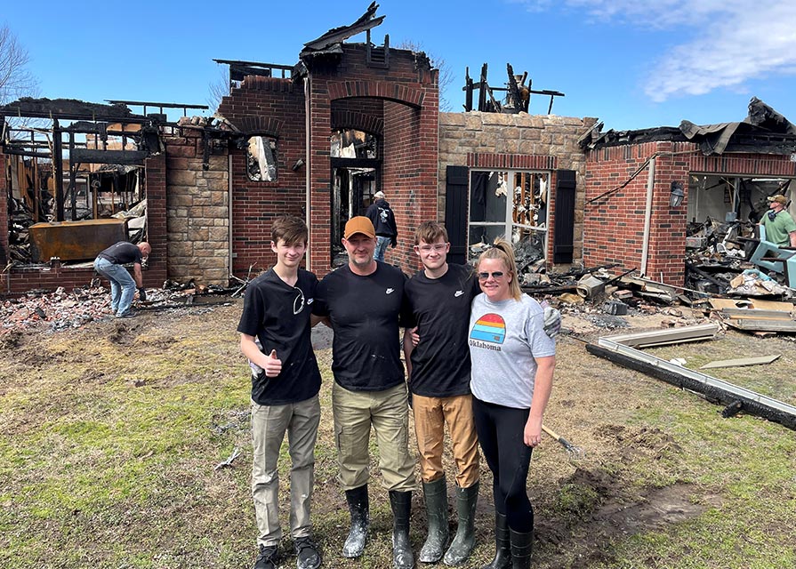 Woman stands with family in front of a burned house